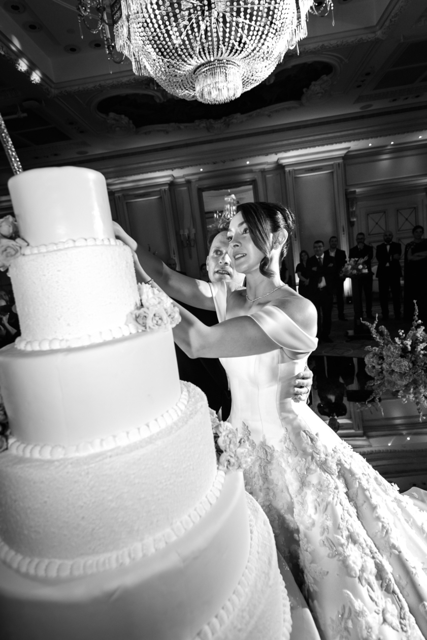Bride and groom cutting a grand wedding cake under a crystal chandelier in Paris, photographed by Olivier Neuville.
